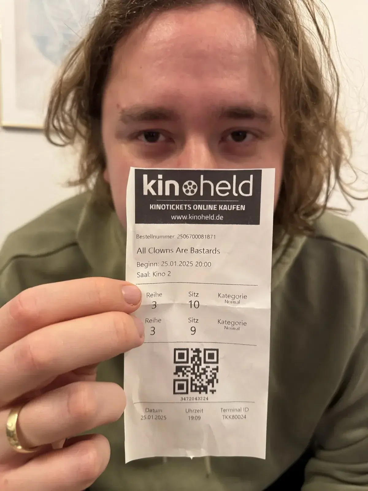 Erik Weise lying on his back, holding up a cinema ticket for “All Clowns Are Bastards”